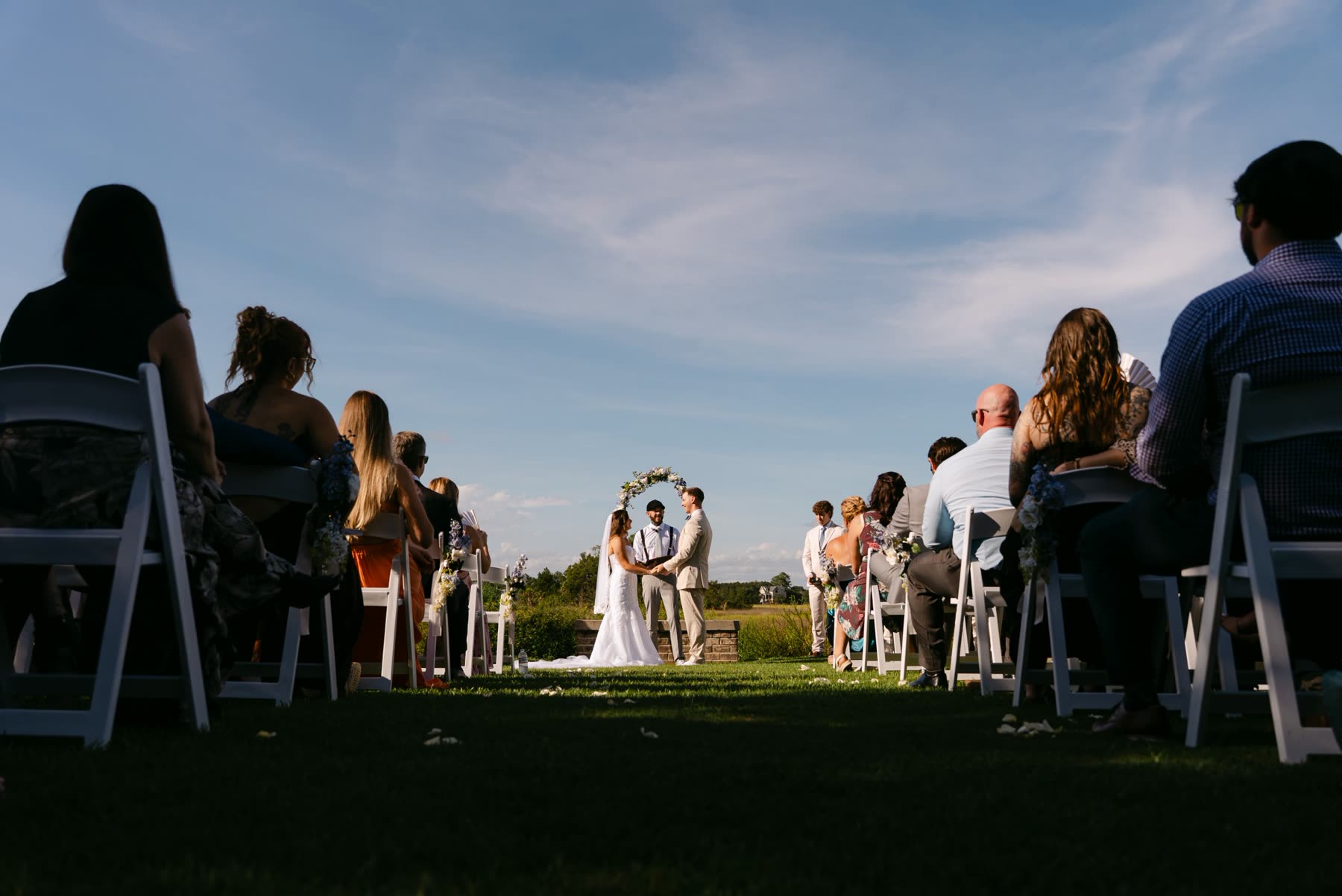 Outdoor ceremony under a big blue sky, guests seated along the aisle