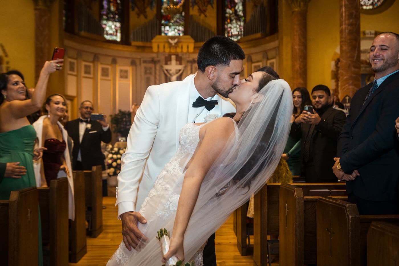 Groom dips the bride for a kiss in a church aisle as guests cheer