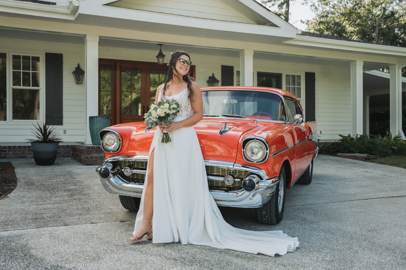 Bride beside a red vintage car in front of a white house