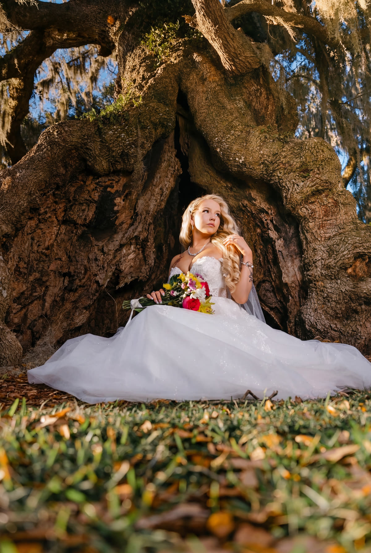 Bride seated at the base of a giant live oak with a bright bouquet