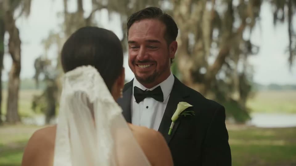 Groom smiling at his bride under live oaks during a first look